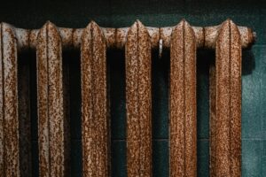 Close-up of a rusty old radiator with textured surface against green tiles, revealing industrial decay.